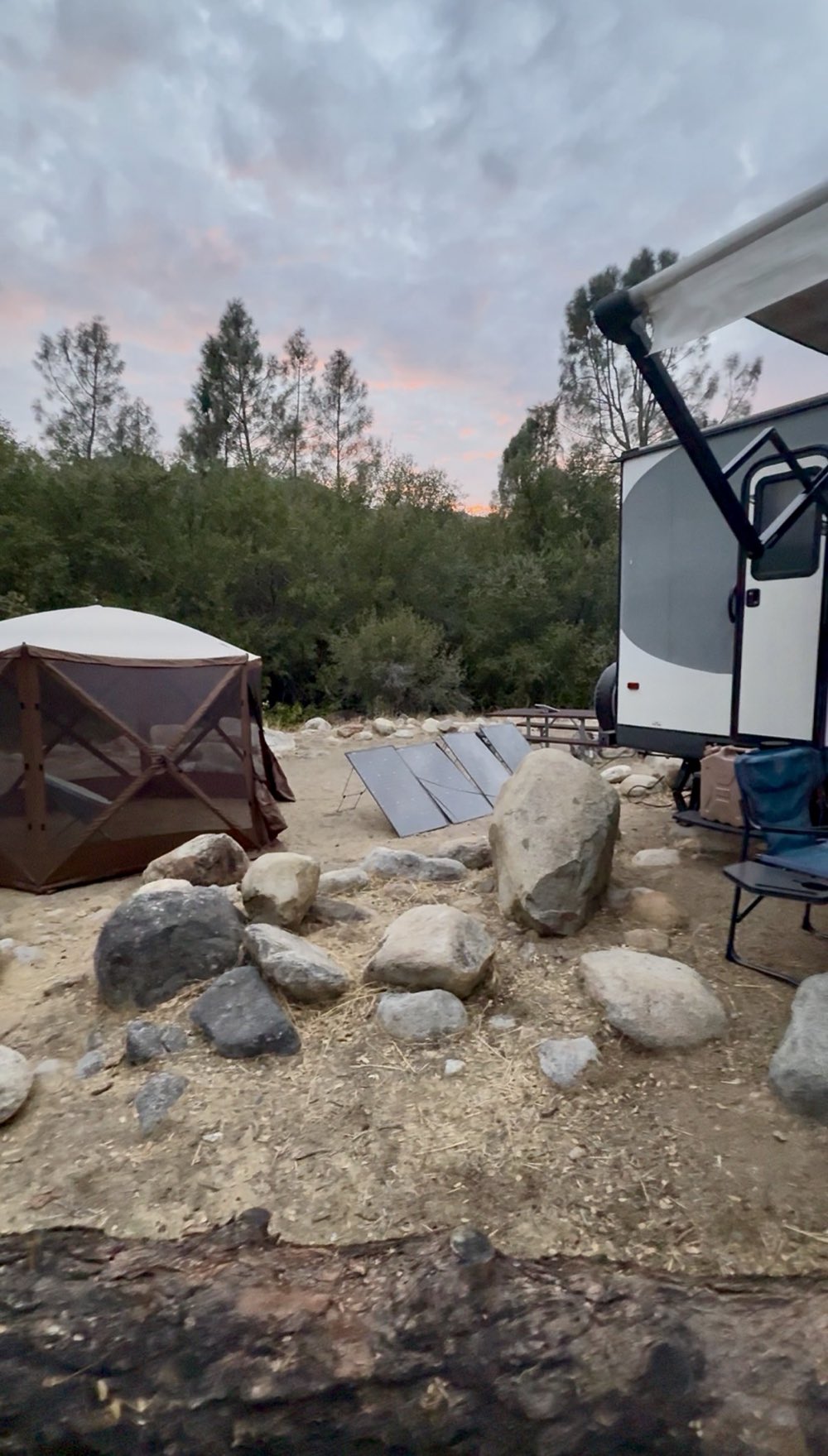 Campsite at dusk with three EcoFlow solar panels set up on the ground beside the Jayco Jay Feather travel trailer, a screen gazebo, and camp chairs